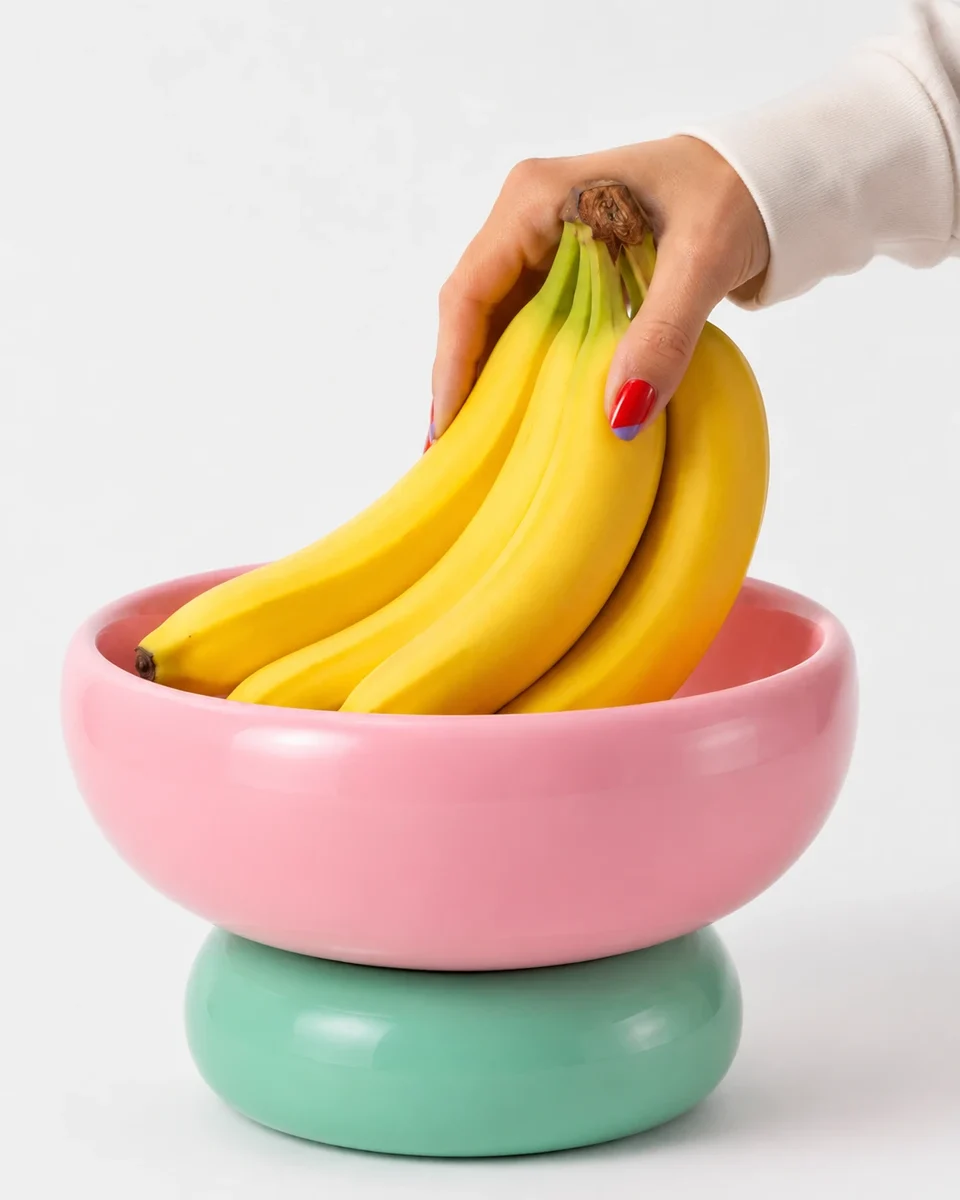 A pink bowl on a mint base holding a bunch of bananas